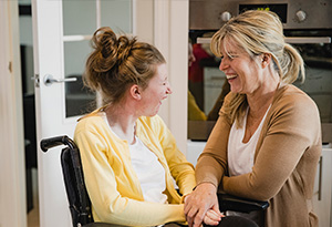 A carer laughs with a young woman in a wheelchair